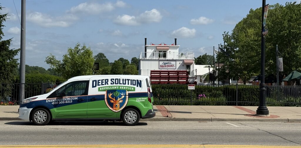 Colorful Deer Solution pest-control van parked on a street with a white show boat building and red seating in the background behind it.