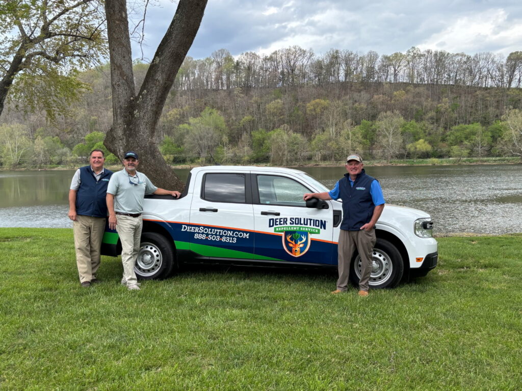 Three Certified Deer Damage Experts from Deer Solution stand beside their branded vehicle